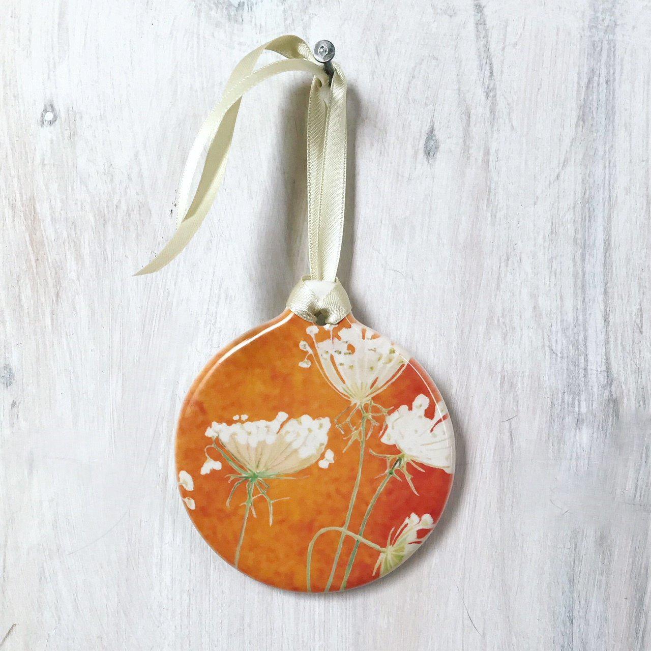 Round ornament with Queen Anne's lace flowers on burnt orange background hanging on cream ribbon