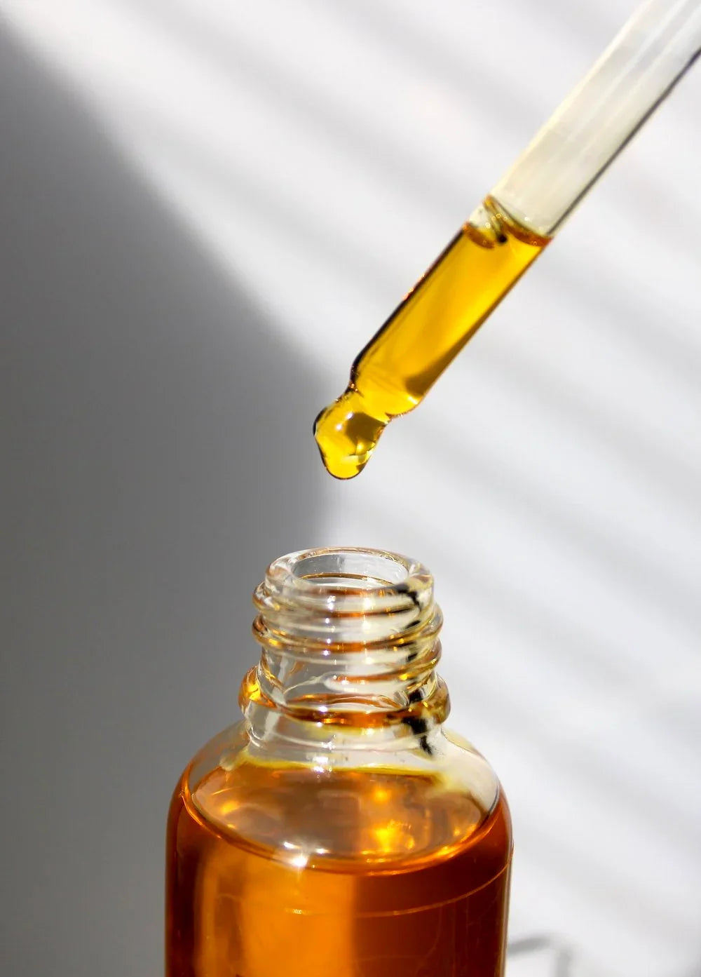 Amber dropper bottle with golden facial oil, sunlight, sustainable beauty at Qu!rk Boutique