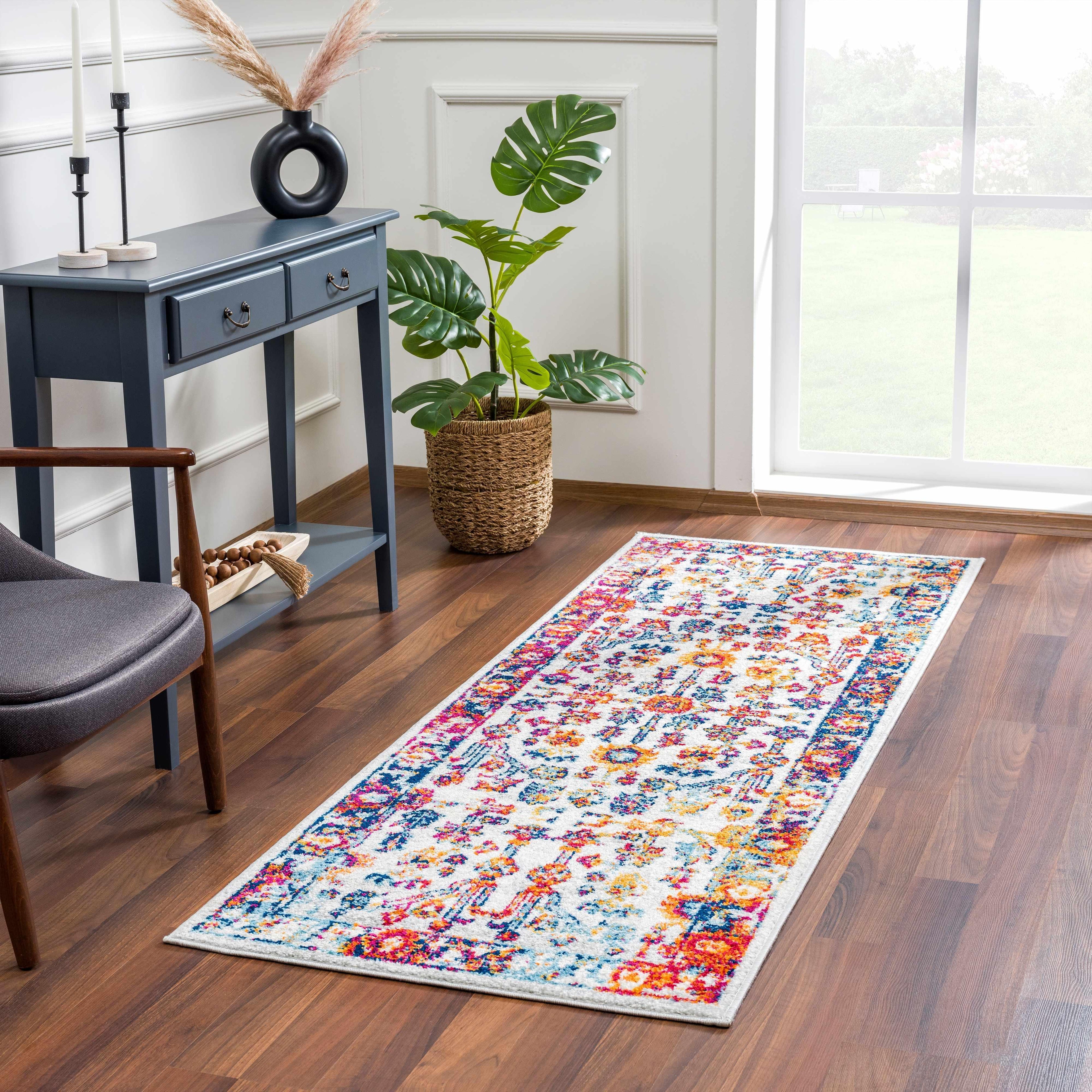 Bright floral hallway runner rug in modern room with wood floors, blue console table, and potted plant.