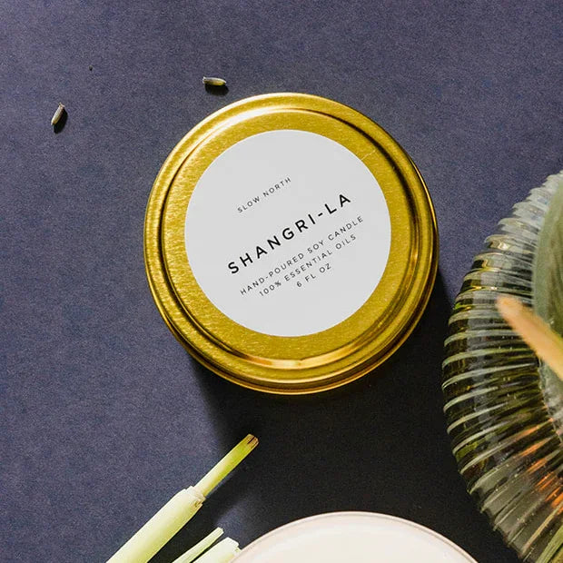 Shangri-La 6oz soy candle in gold tin by Slow North on dark background, shown at Qu!rk Boutique.