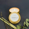 Shangri-La hand-poured soy candle from Slow North in gold tin, surrounded by botanicals.
