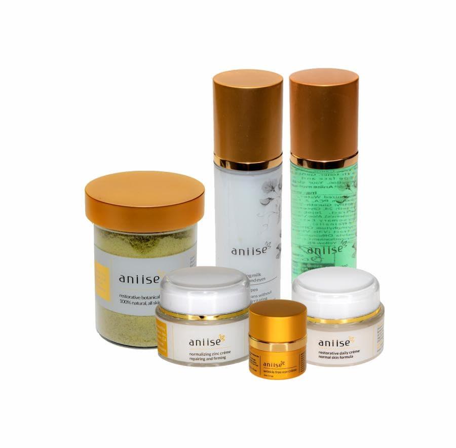 Anise skincare collection set with gold lids, featuring creams, cleanser, and botanical scrub.