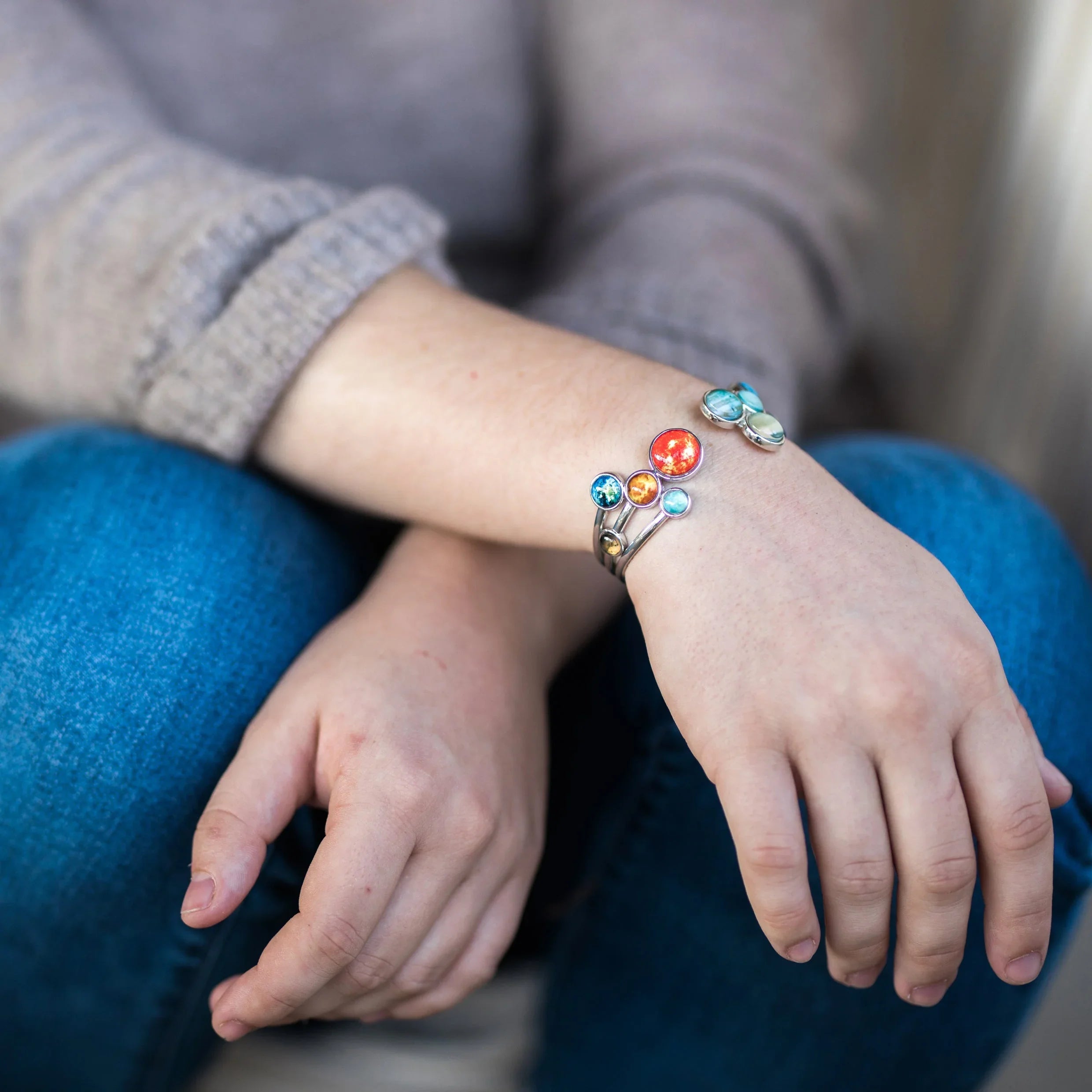 Solar system planet bracelet worn on wrist with blue jeans and gray sweater