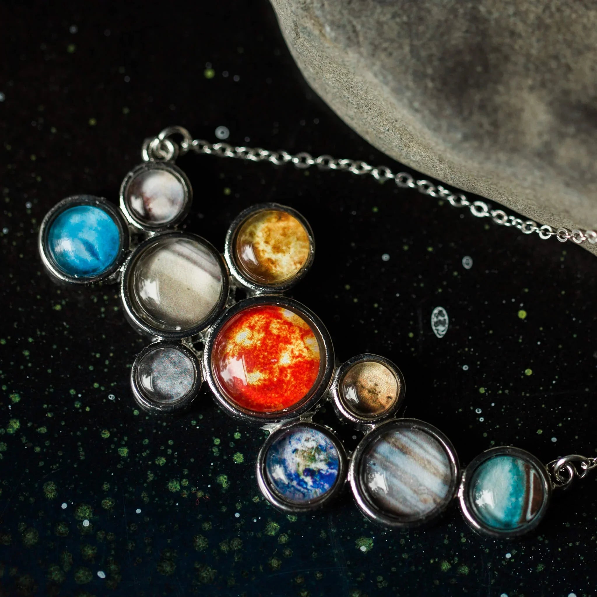 Close-up of a silver necklace pendant with planets of the solar system on a cosmic background