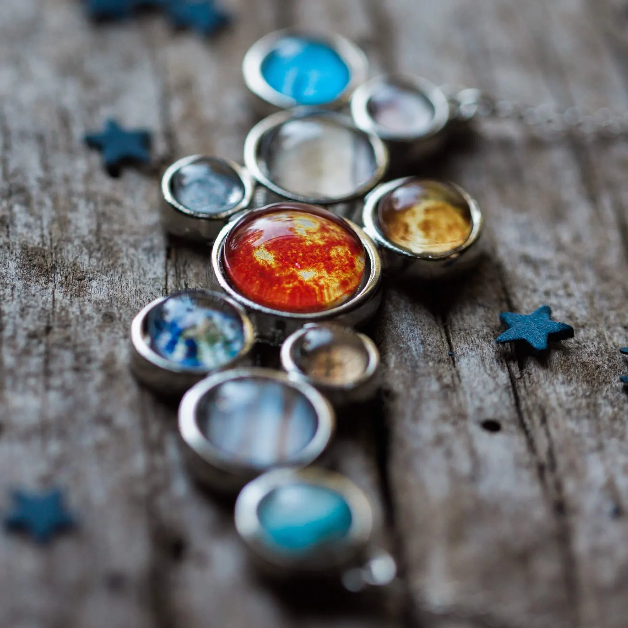 Close-up of a solar system pendant necklace with colorful planet charms on rustic wood