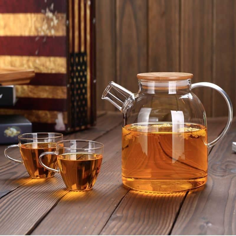 Glass teapot with wooden lid and tea, two glass cups on rustic wood table, cozy home decor