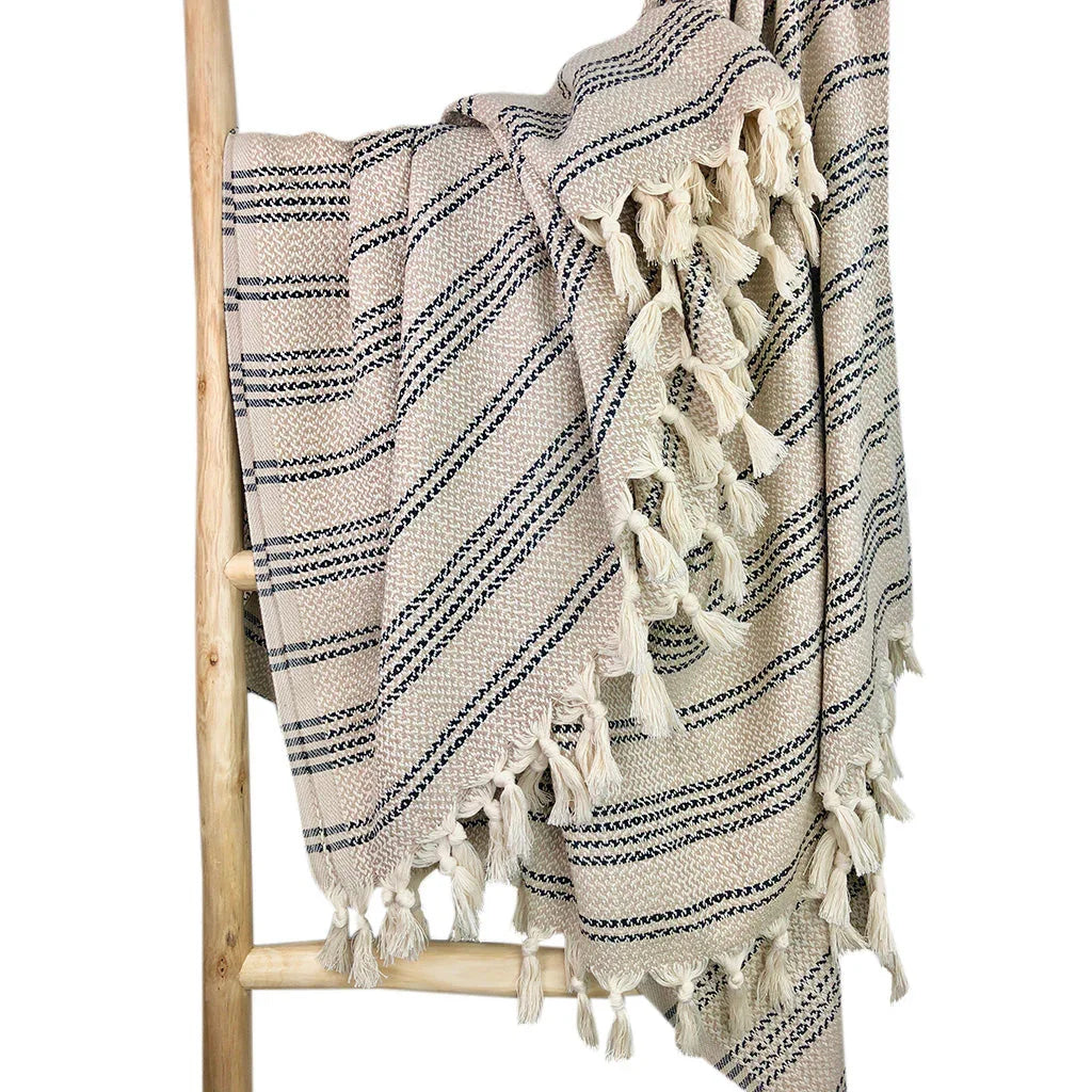 Striped Turkish throw blanket with tassels draped over a wooden ladder, cozy and artisan-crafted.