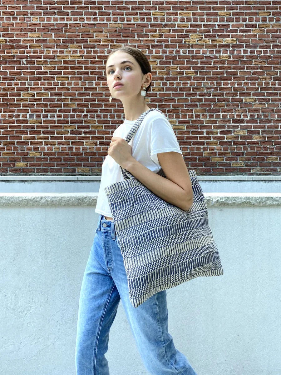 Woman with eco-friendly blue woven tote bag, white shirt, and jeans at Qu!rk Boutique