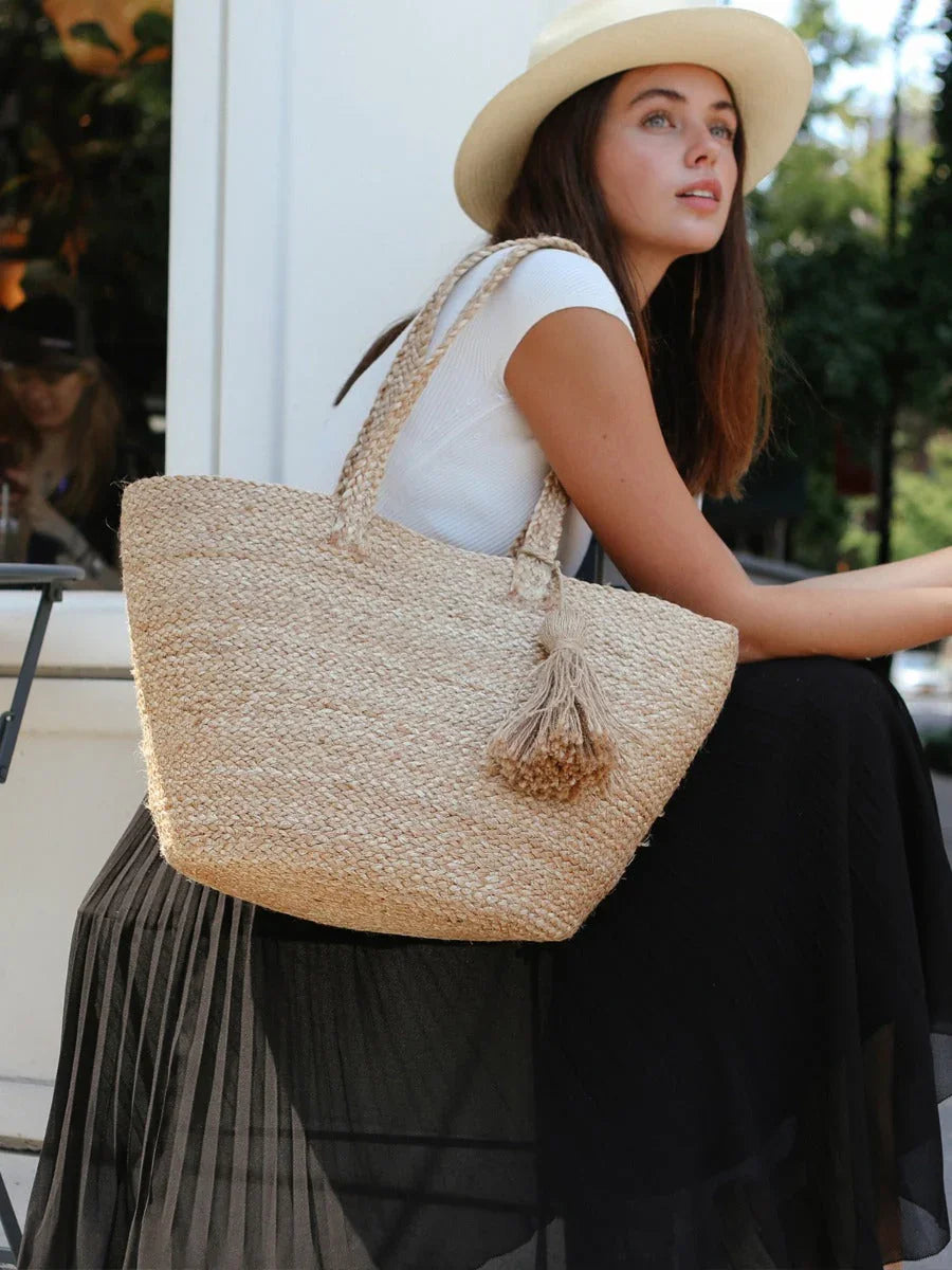 Woman wearing a hat holding a woven straw shoulder bag with tassel, outdoor boutique style