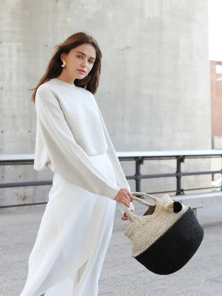 Woman in chic winter white outfit holding black and tan woven bag, Qu!rk Boutique style