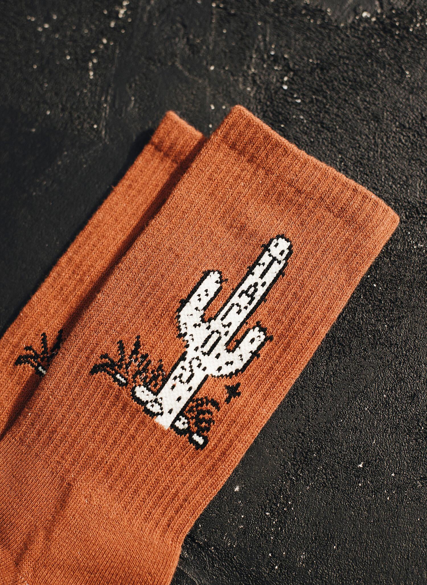 Rust-colored socks with white and black pixelated cactus design on textured black surface