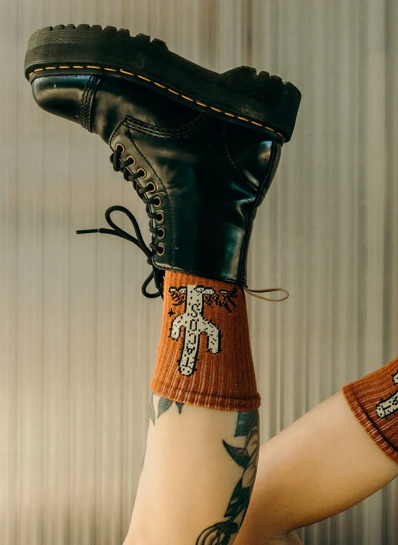 Legs with tattoo wearing rust orange cactus patterned socks and black platform combat boots