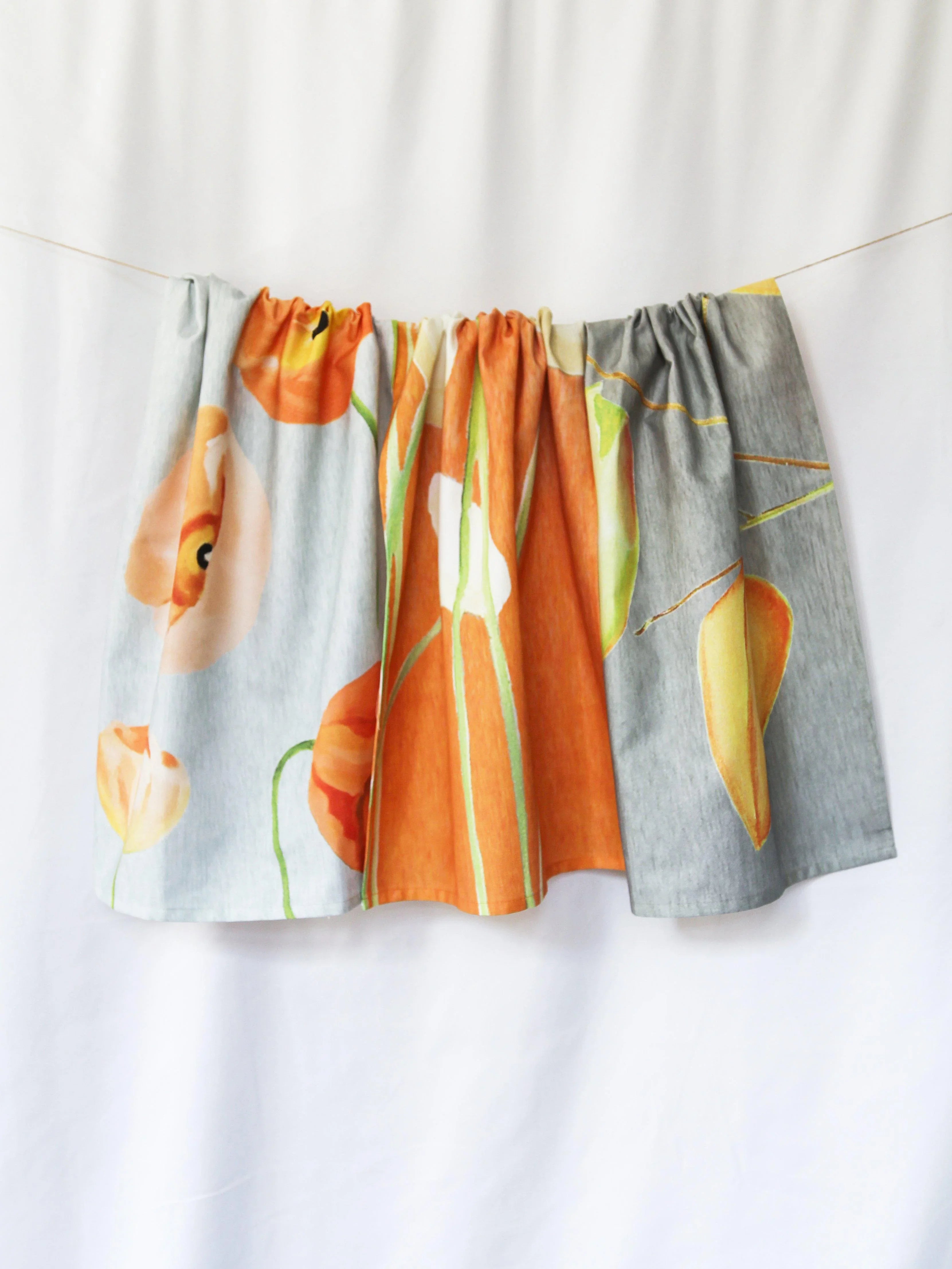 Cream tea towel with orange and yellow floral and pear designs hanging on a string
