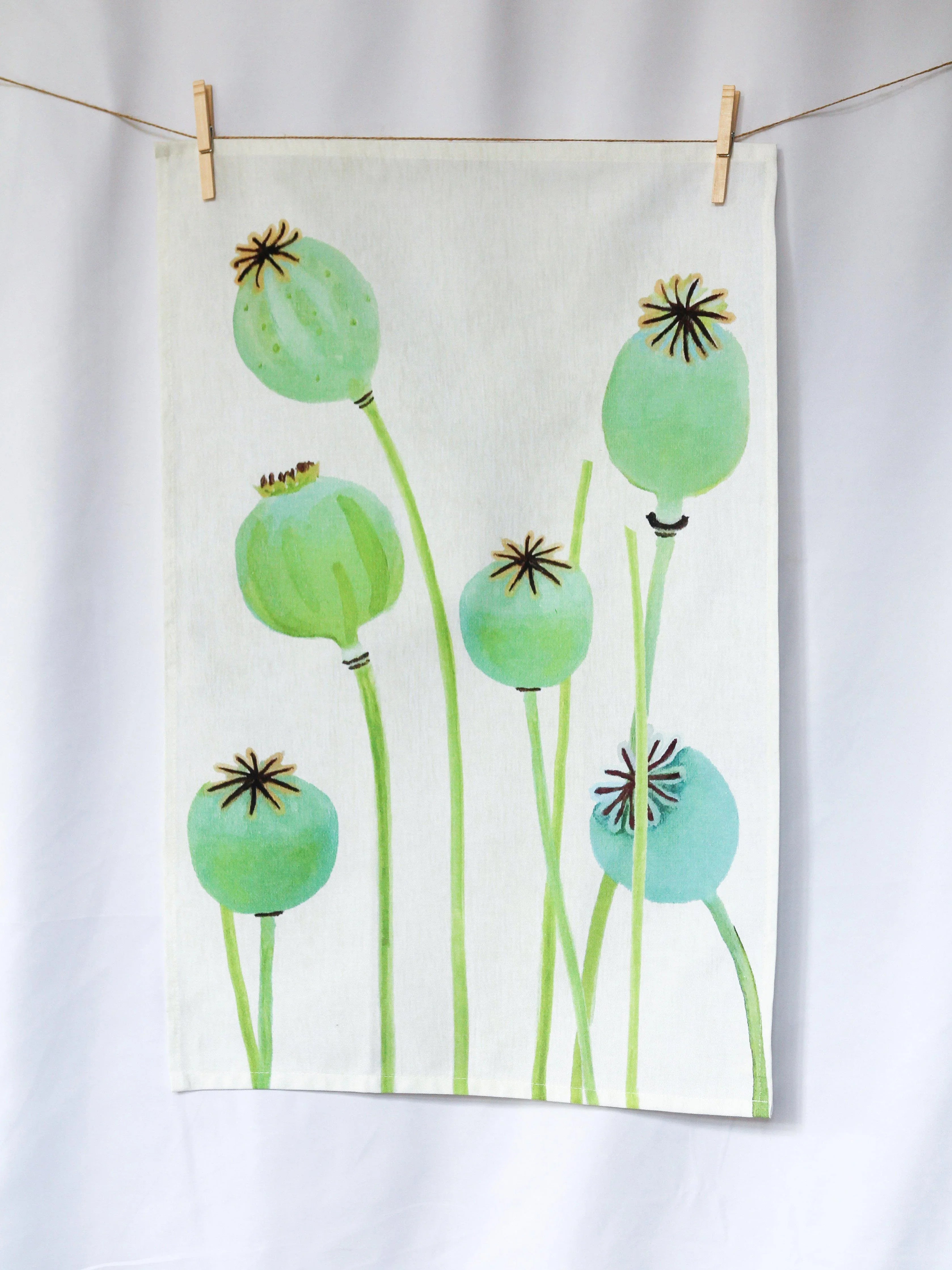 Ecru tea towel hanging on a line with green poppy pod botanical print