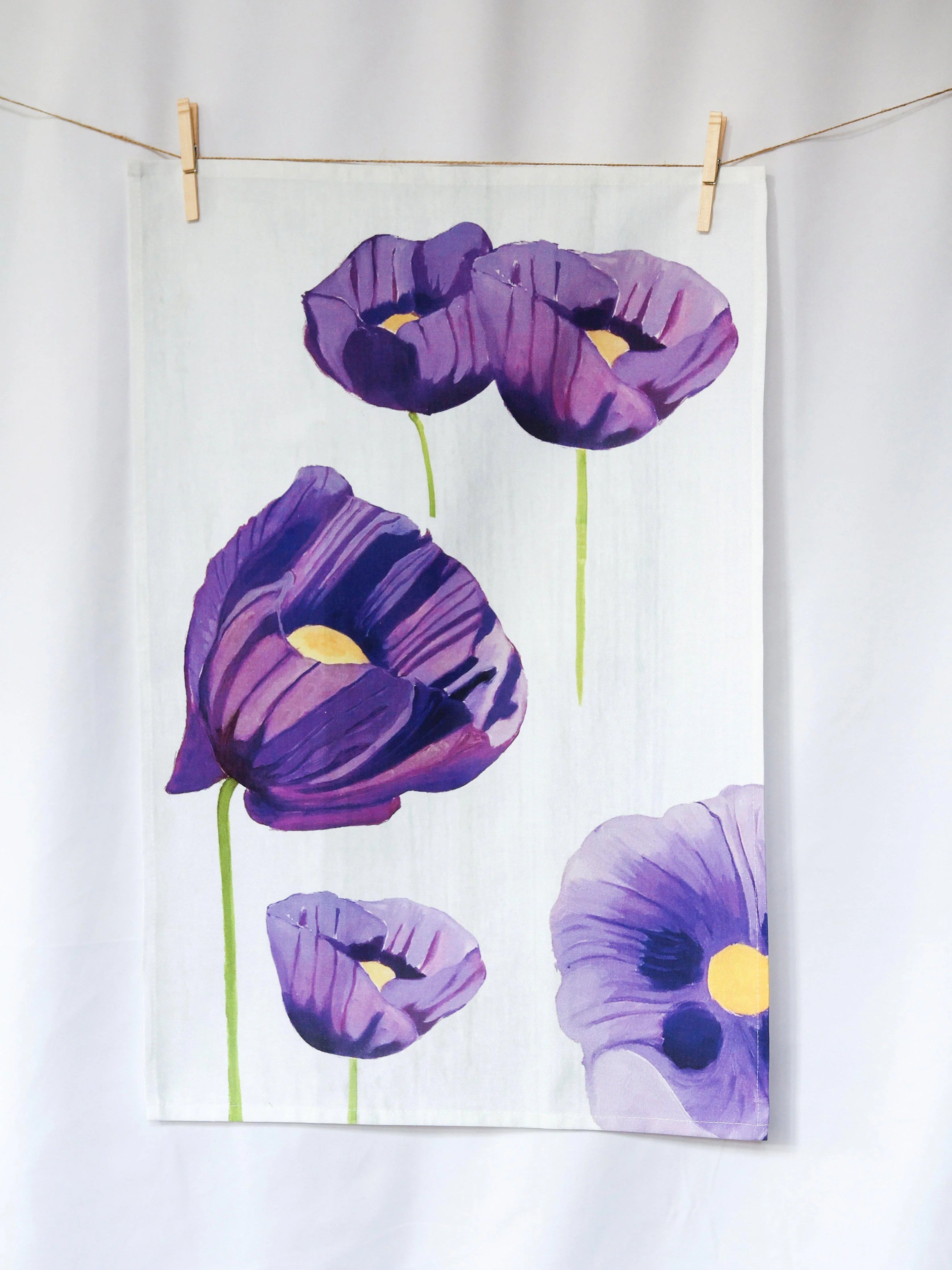 White tea towel hanging with purple poppy flower prints and green stems