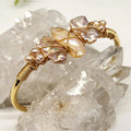 Gold wire-wrapped bangle with iridescent baroque pearls, displayed on clear quartz crystals.