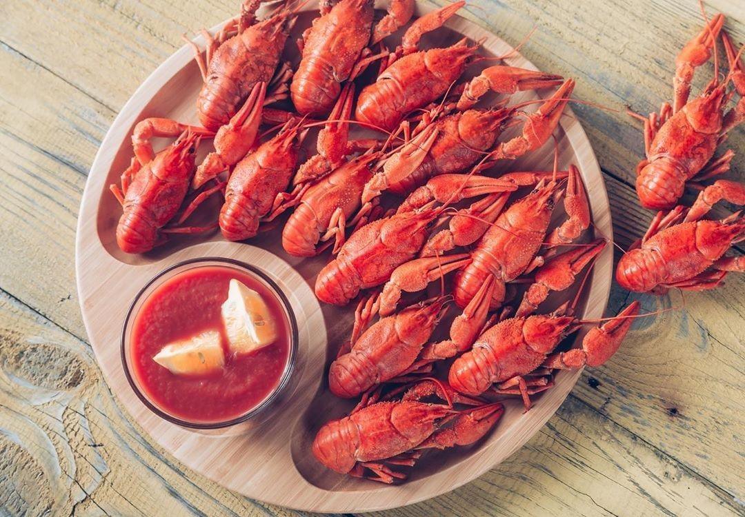 Plate of boiled crawfish with cocktail sauce and lemon wedges on rustic wood table