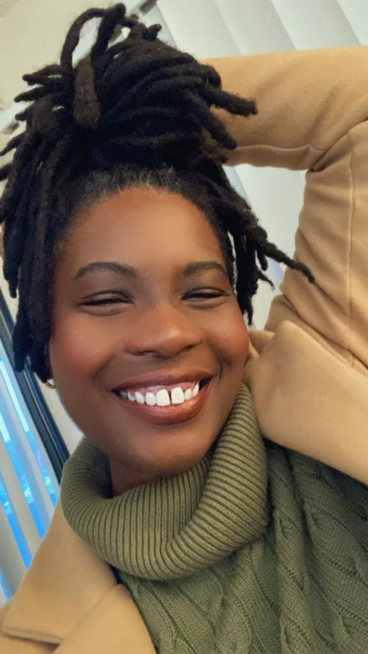 Smiling woman in a green turtleneck sweater and tan coat, celebrating Qu!rk Boutique style