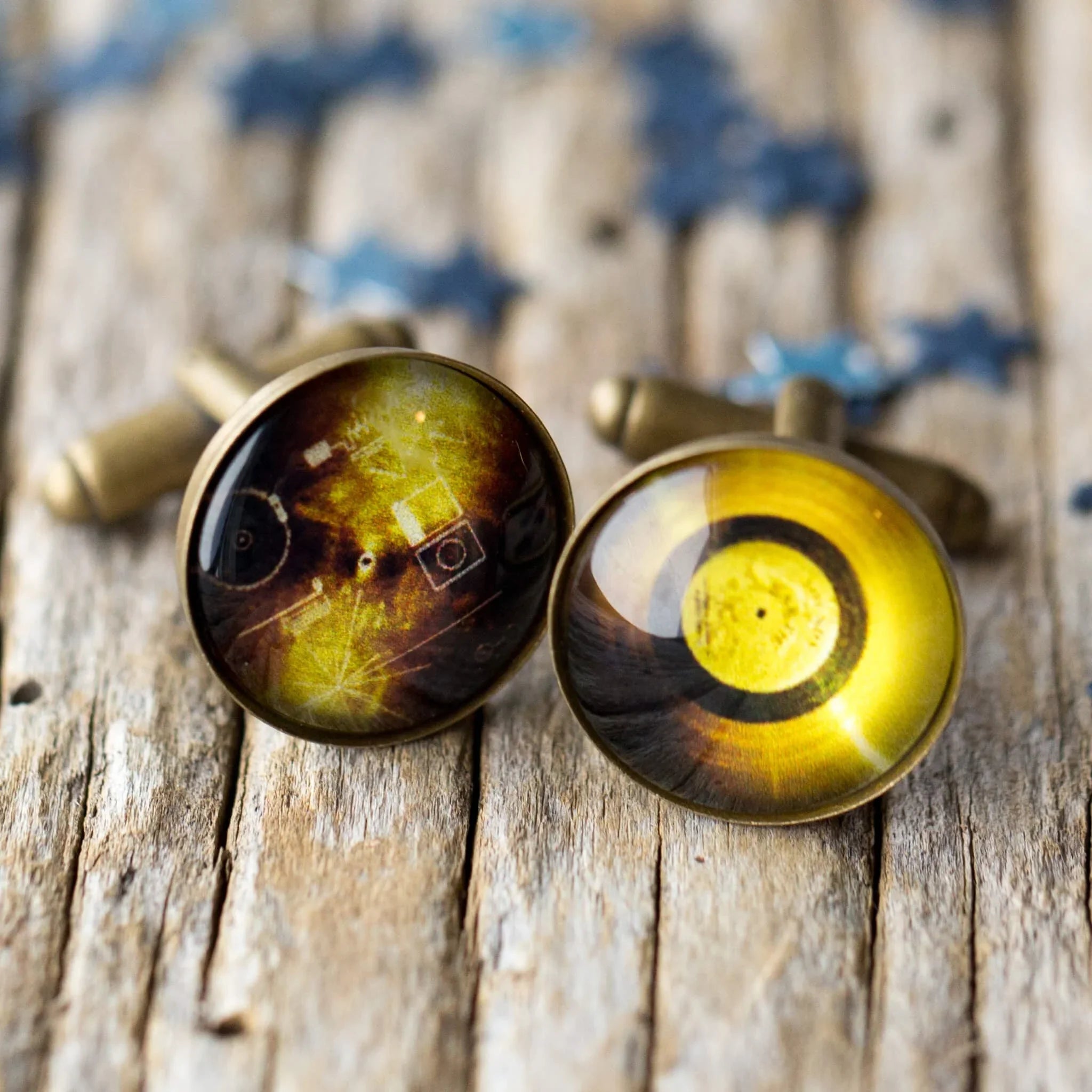 Vintage brass cufflinks with yellow and dark abstract circular design on rustic wooden surface