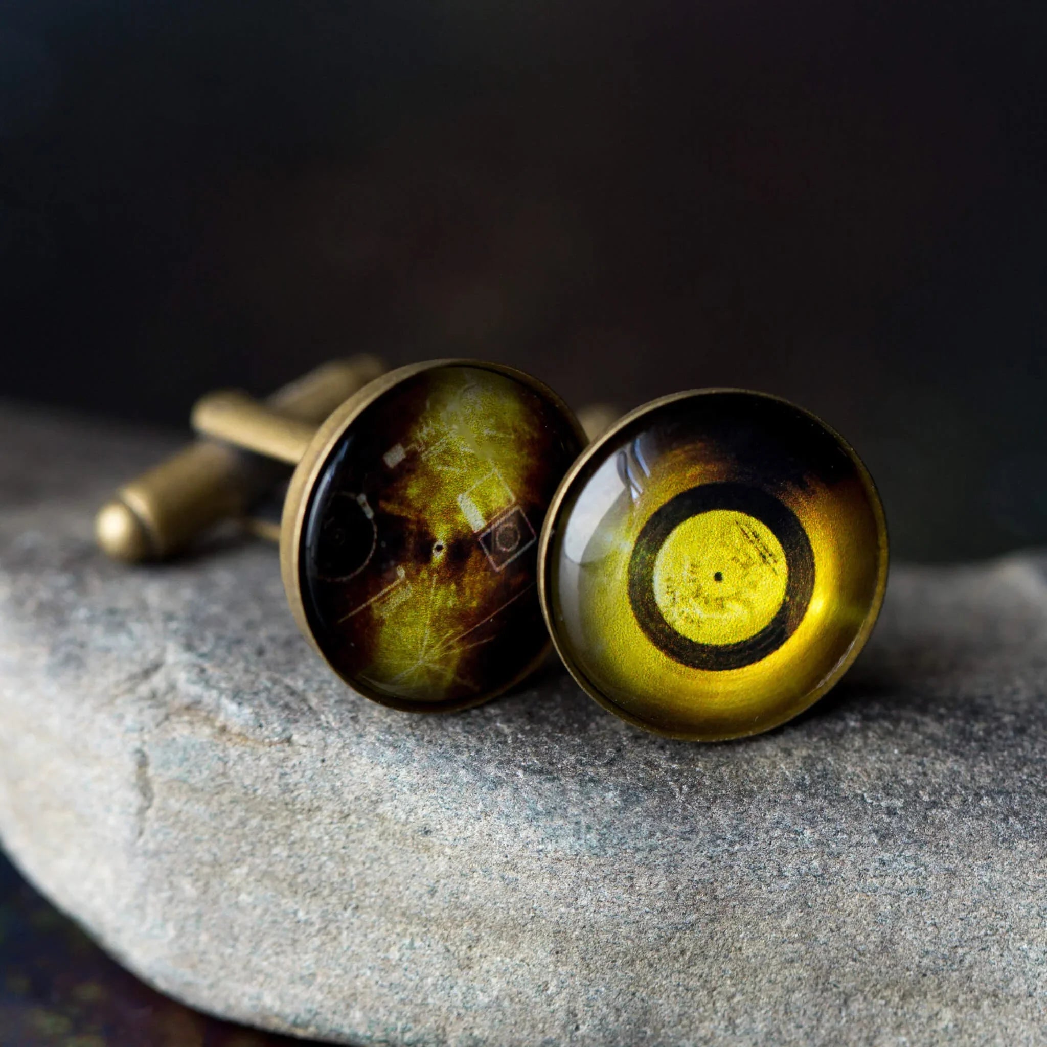 Pair of vintage brass cufflinks with amber-colored round glass faces on stone surface