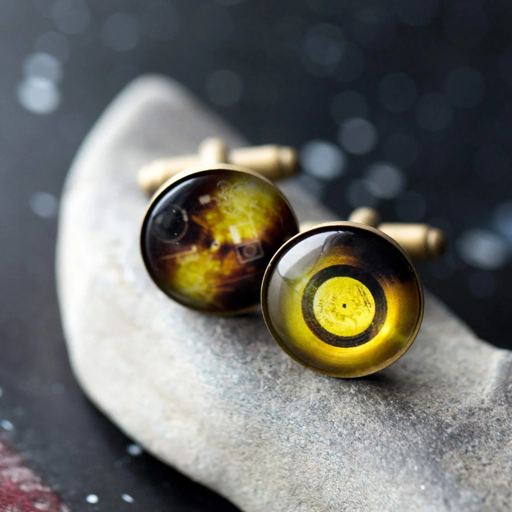 Round vintage-style cufflinks with yellow and black circular patterns on gray stone