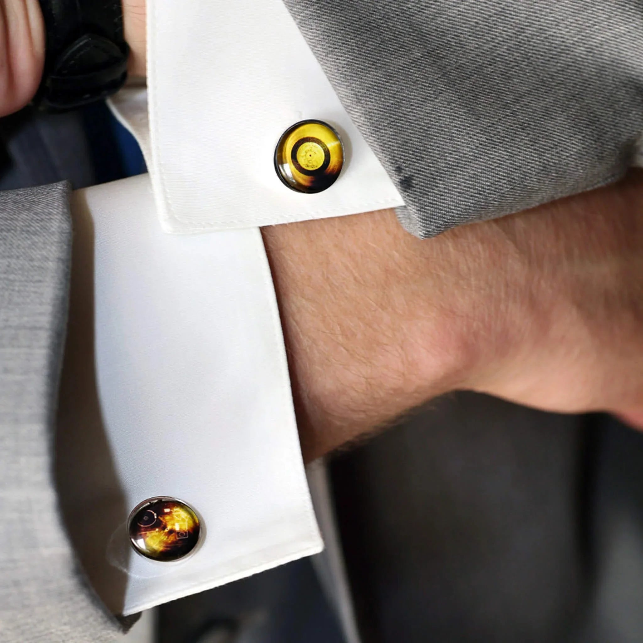 Close-up of a man's wrist wearing white French cuffs with round amber-themed cufflinks and a light gray suit jacket