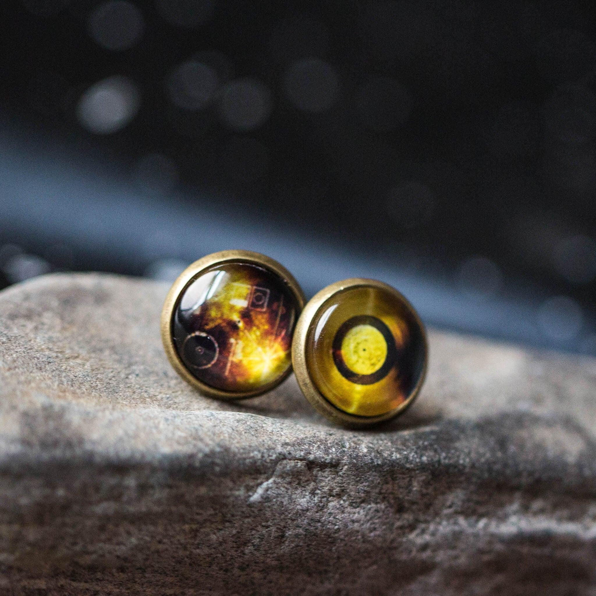 Close-up of two round steampunk cufflinks with gear and circular designs on stone surface