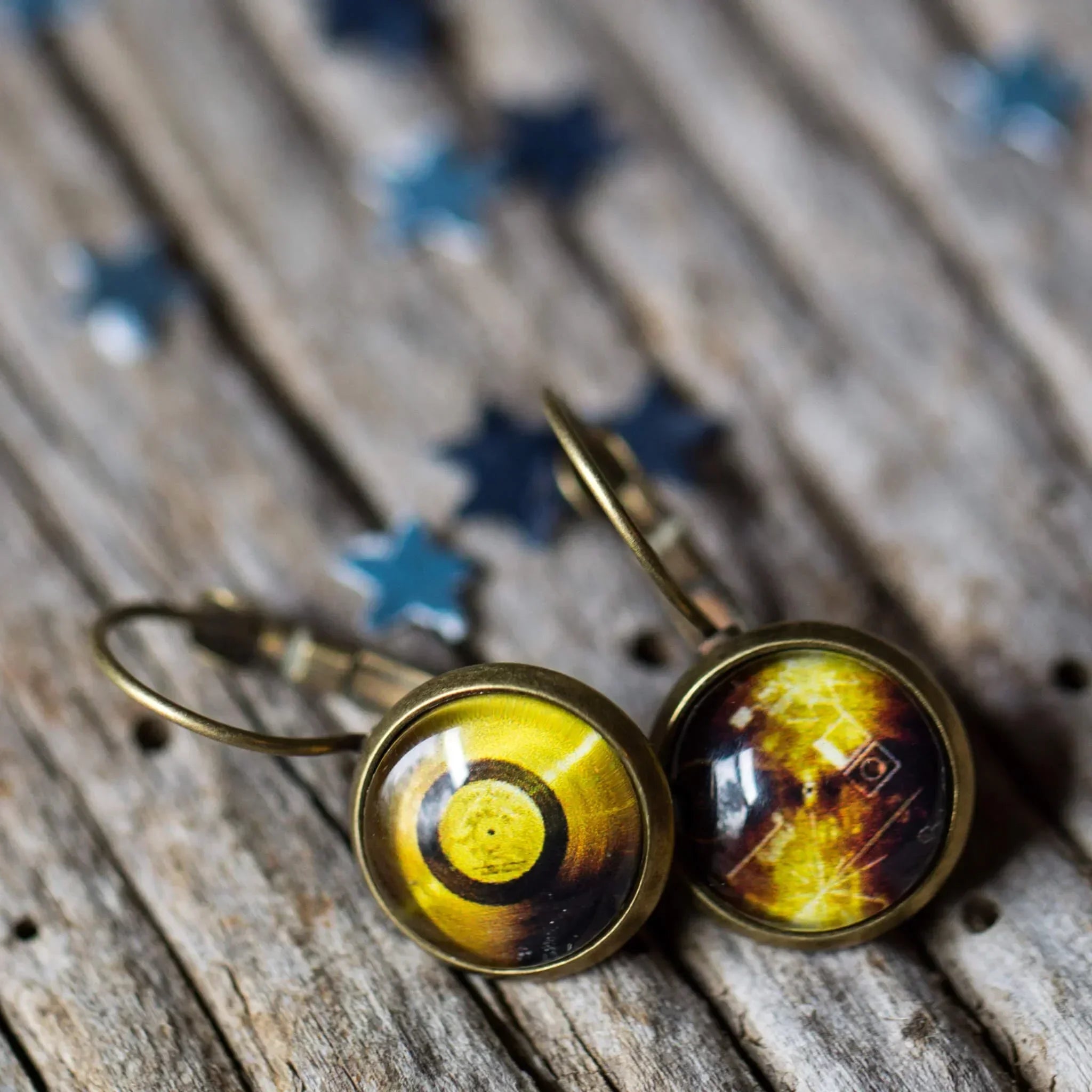 Close-up of vintage brass earrings with yellow and brown circular designs on rustic wooden surface with blue star confetti