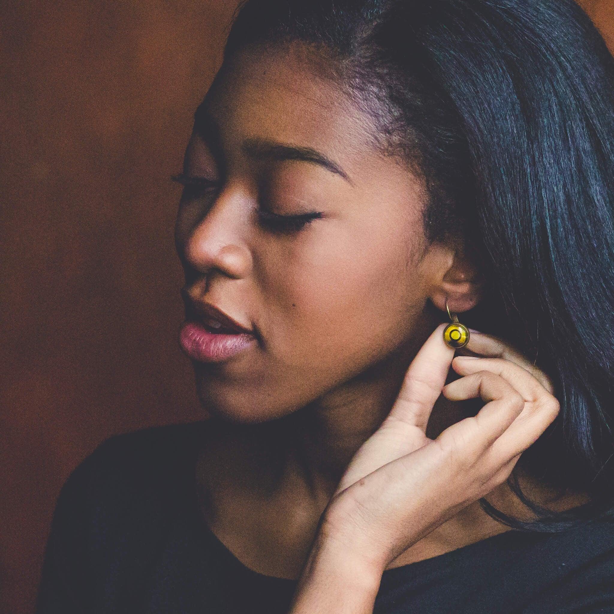 Close-up of woman with closed eyes touching yellow circular earring on dark background