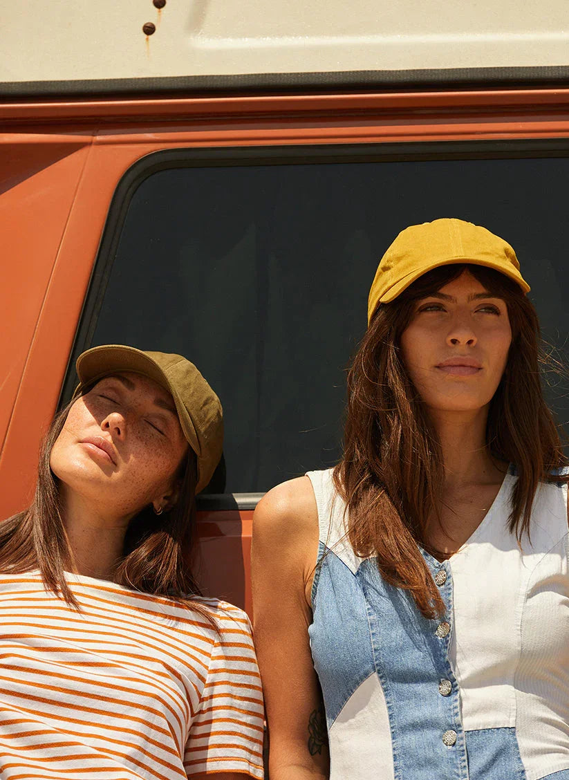 Two women wearing vintage washed dad hats, standing outdoors by an orange vehicle in sunlight