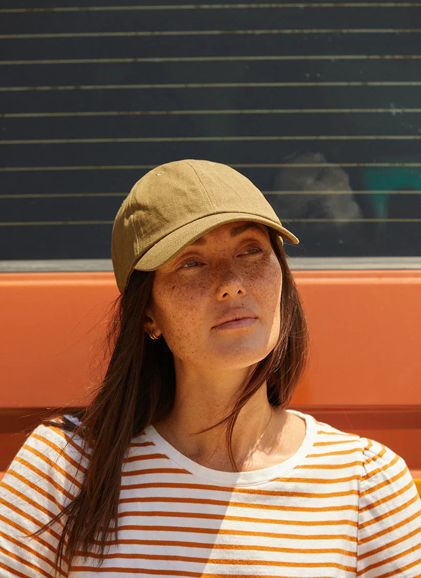 Woman in a vintage washed khaki dad hat and striped shirt, outdoor casual style