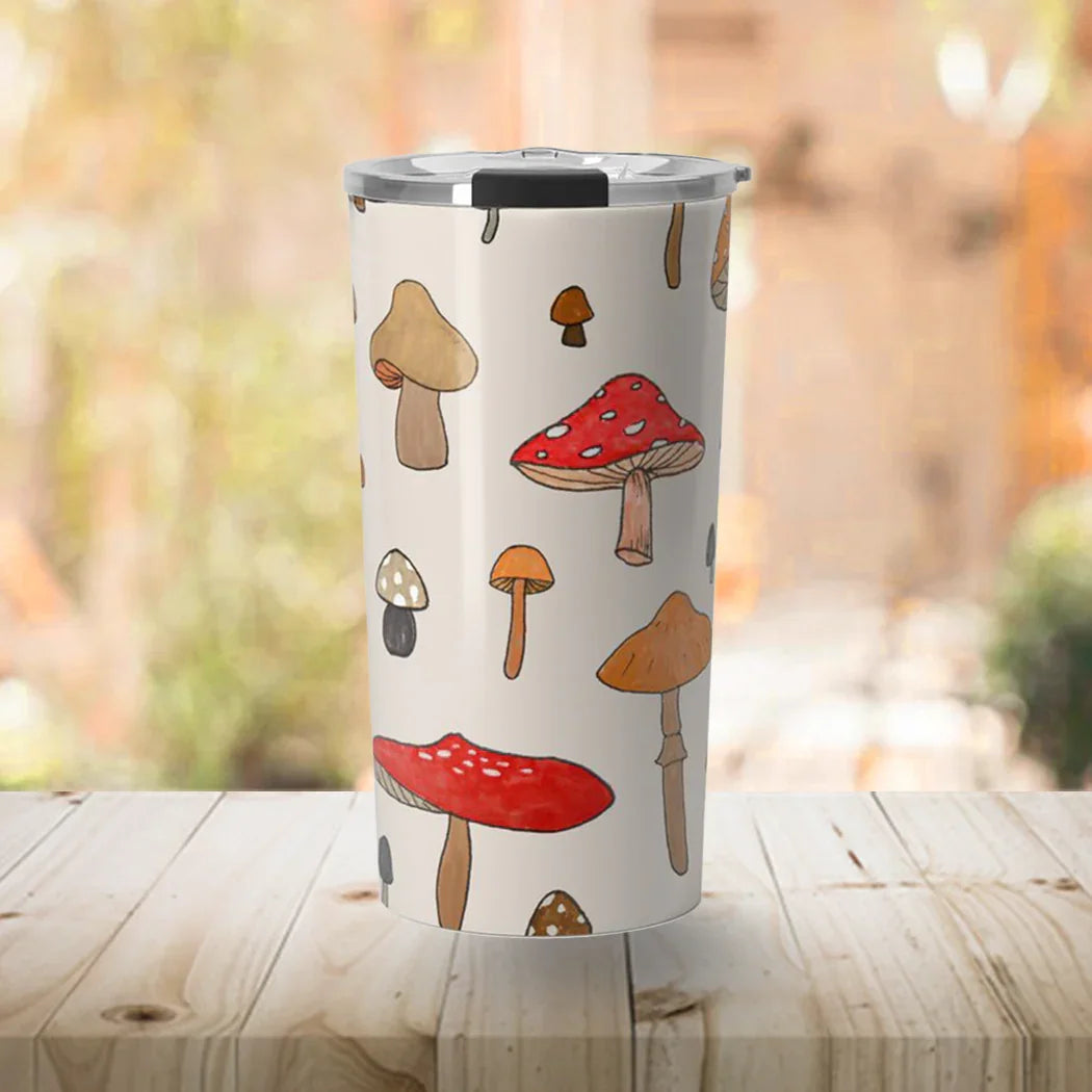 White travel tumbler with colorful cartoon mushroom illustrations on wooden table with blurred outdoor background