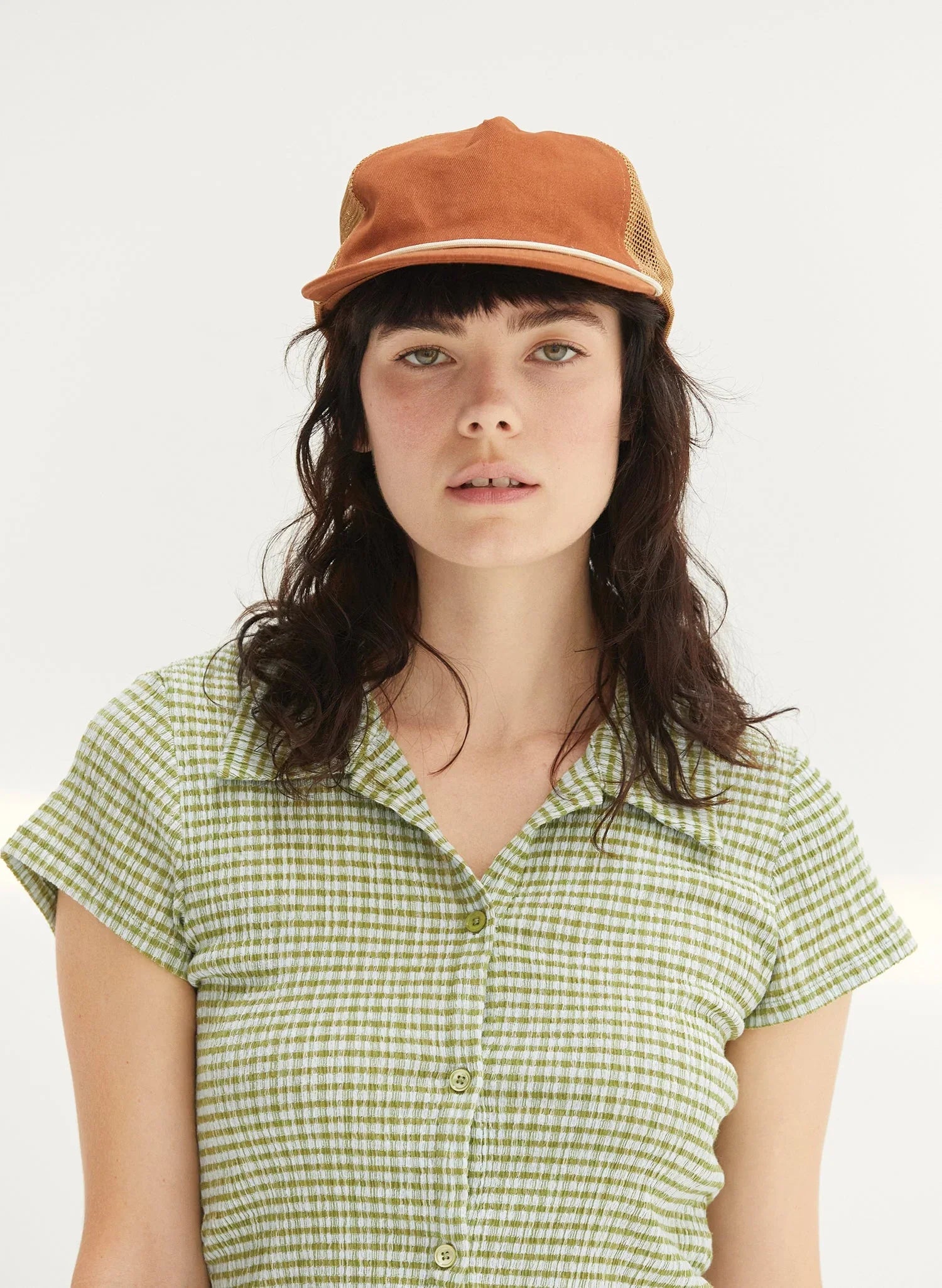 Woman wearing rust brushed cotton rope trucker hat from Qu!rk Boutique, styled with a green plaid shirt.