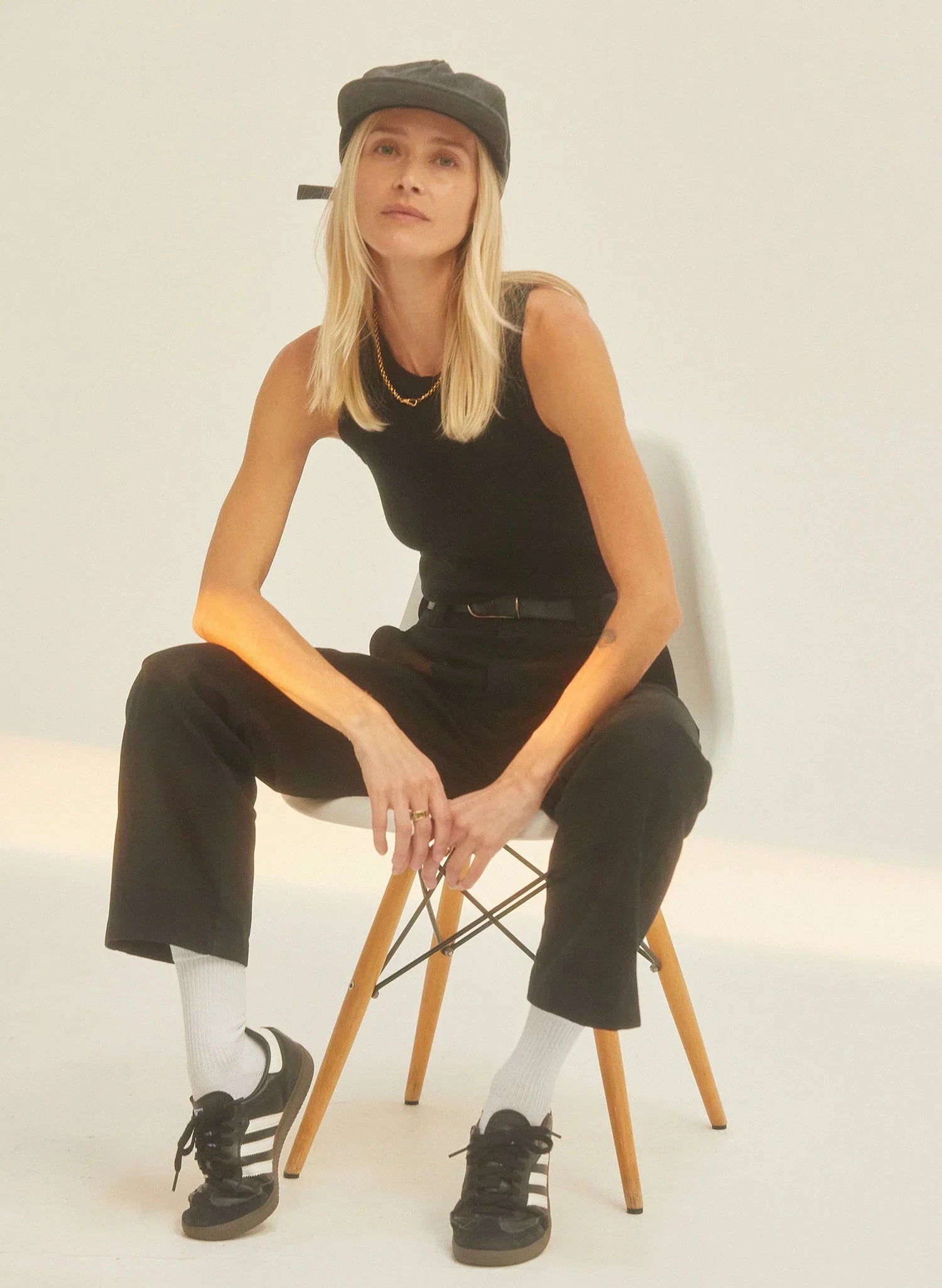 Woman in black vintage washed cotton twill field trip hat, black tank, and black pants, sitting on a chair in a minimalist setting at Qu!rk Boutique.