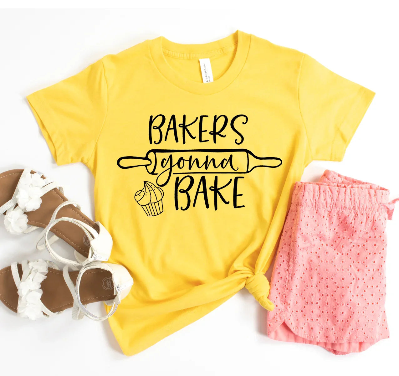 Yellow t-shirt with black text 'Bakers gonna bake' and cupcake graphic, paired with pink shorts and white sandals