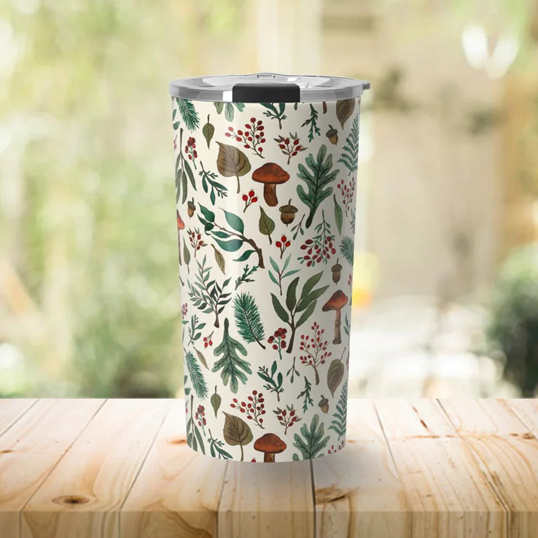 Tall insulated tumbler with forest-themed design of leaves, mushrooms, and berries on wooden table