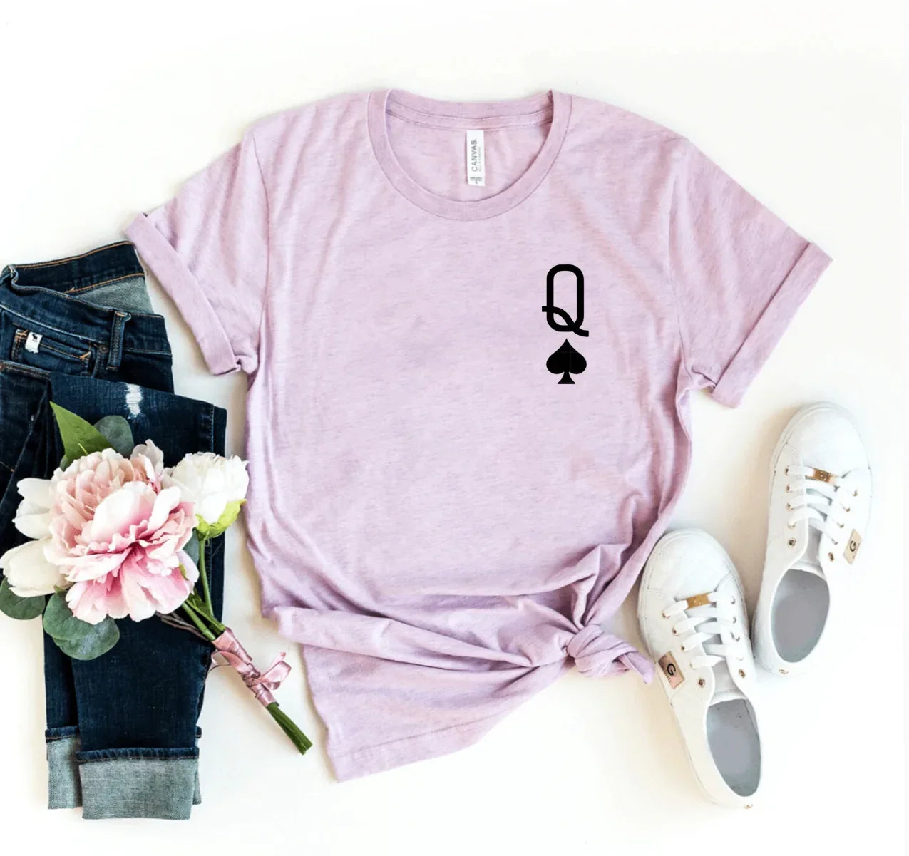 Lilac t-shirt with black Queen of Spades print, paired with rolled denim jeans, white sneakers, and pink flowers