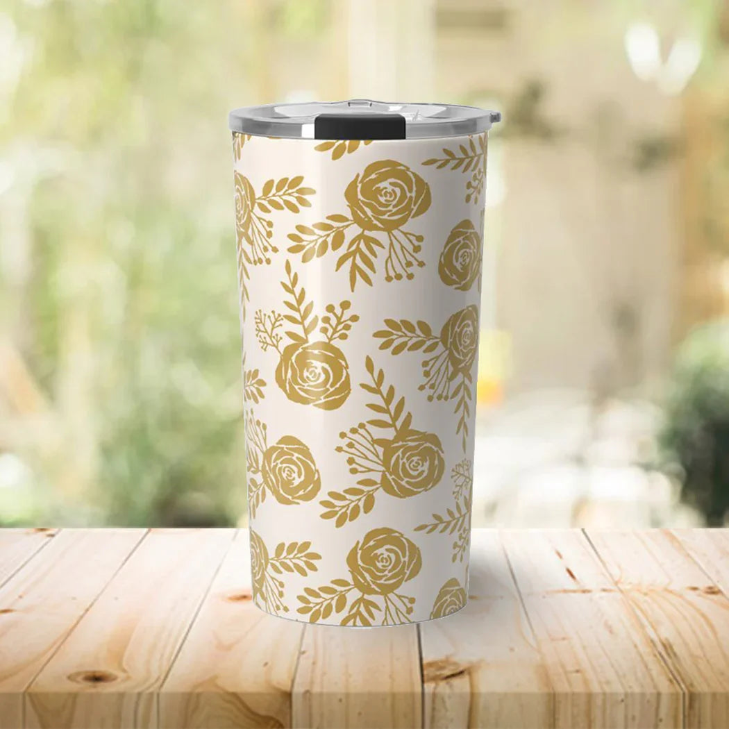 White travel tumbler with gold floral pattern on wooden table in bright indoor setting