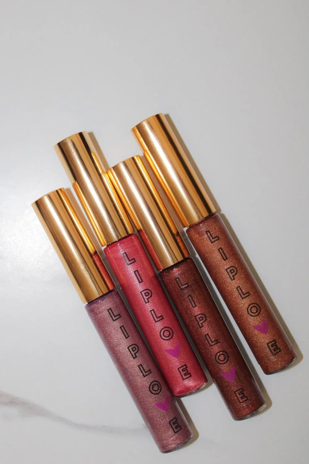 Four Lip Love glitter lip gloss tubes with gold caps on a white background, Qu!rk Boutique