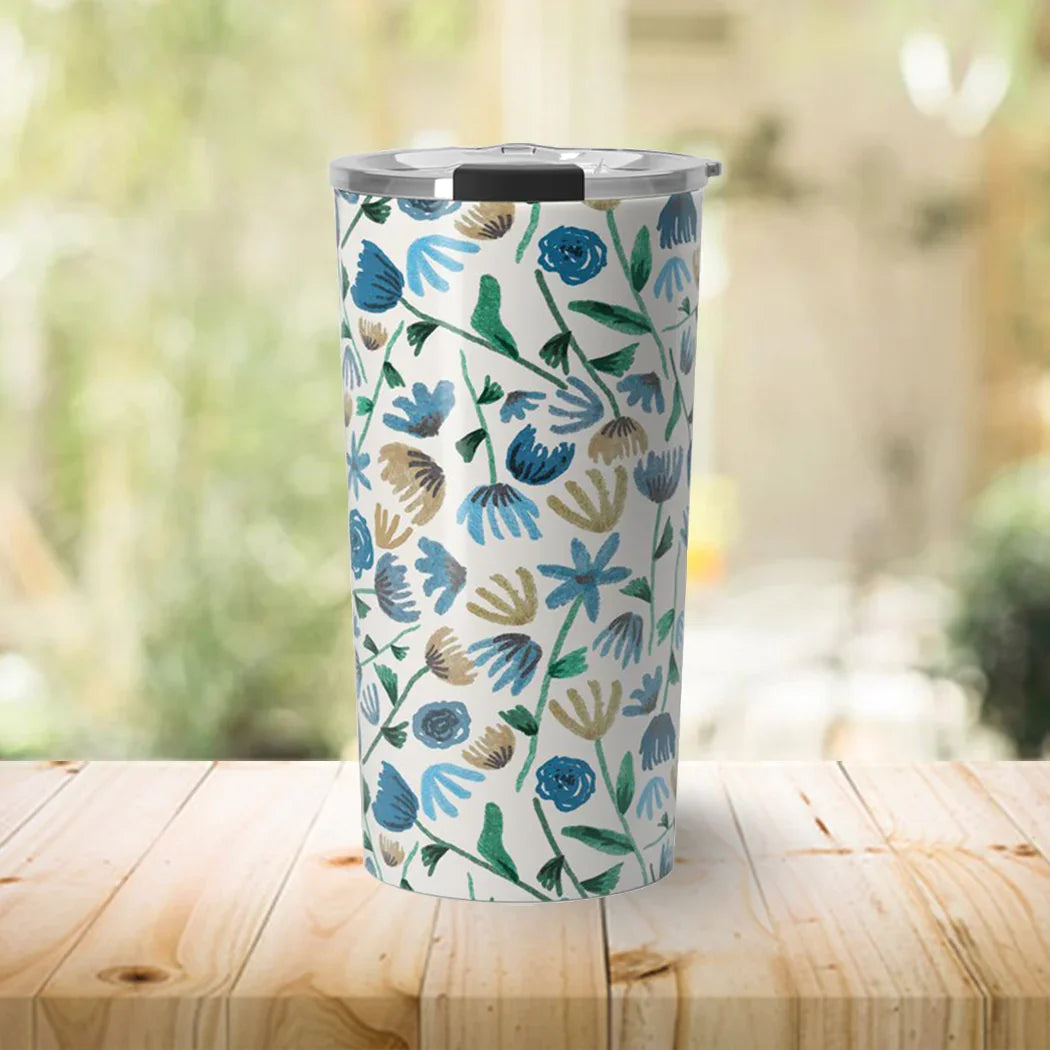 Stainless steel tumbler with clear lid featuring blue and beige floral pattern on wooden table