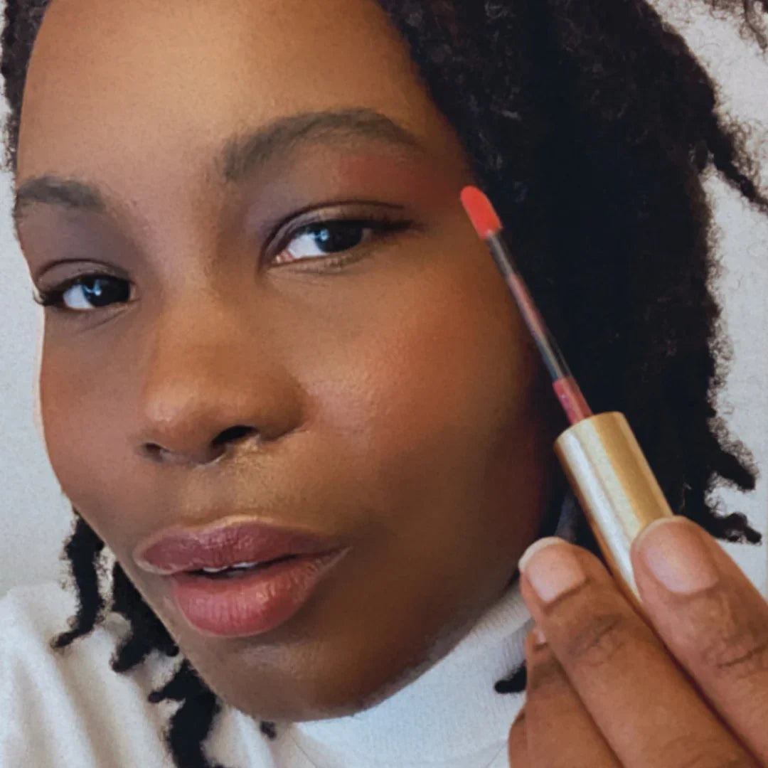 Woman applying pink lip gloss, showcasing ethical beauty at Qu!rk Boutique & Gift Shop